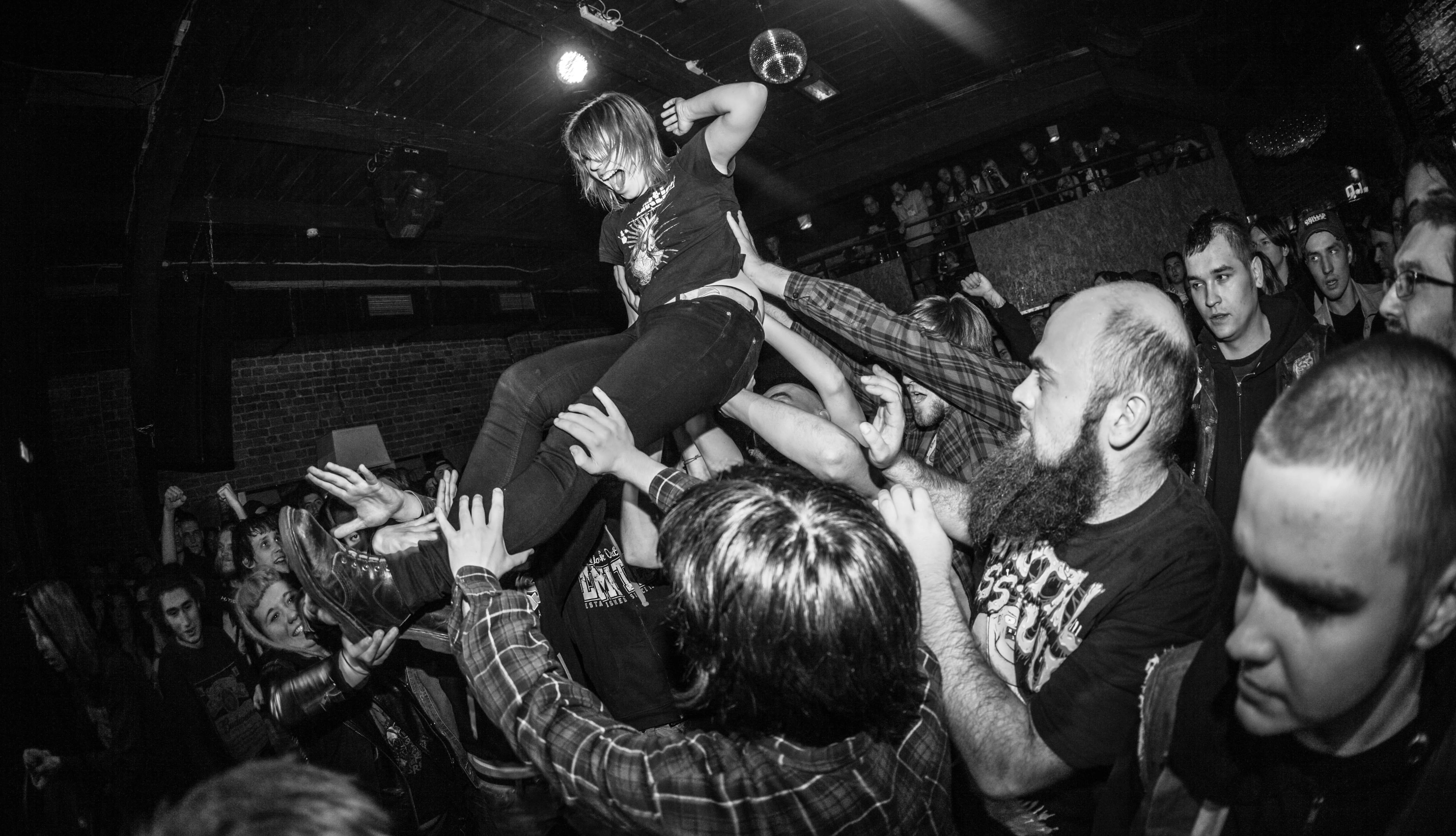 Schwarz-Weiß-Konzertfoto: Eine Person wird lachend crowdsurfend von der Menge in einem Punk-Club getragen.